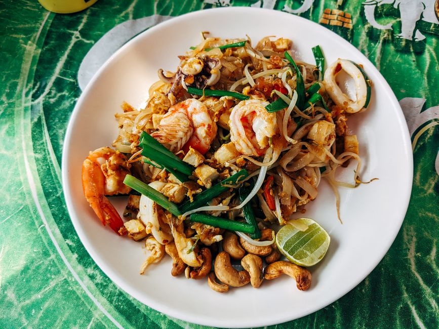 Close-up of Pad Thai with shrimp, vegetables, and lime served on a ceramic plate in Bangkok.